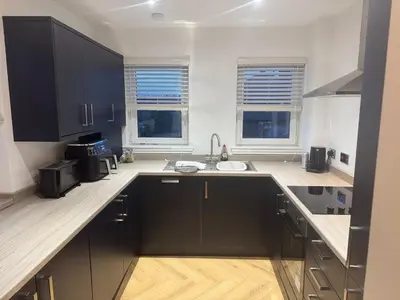 a kitchen with black cabinets and a sink and two windows at Stylish modern flat in the centre of Dunfermline in Dunfermline