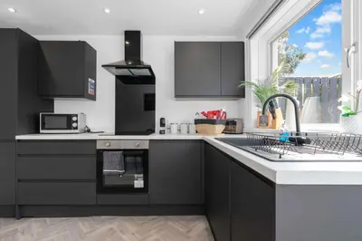 a kitchen with black cabinets and a sink and a window at Livingston Retreat 4bed Home Wi-Fi Parking in Uphall