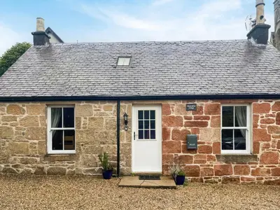 a brick cottage with a white door and windows at Monawilline Cottage in Lamlash