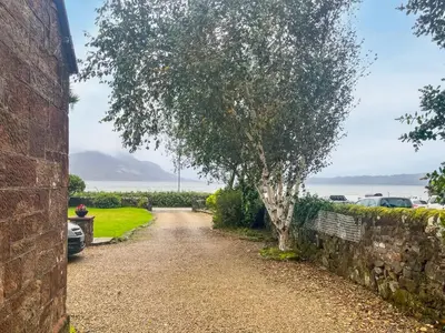 a driveway with a tree and a stone wall at Monawilline Cottage in Lamlash