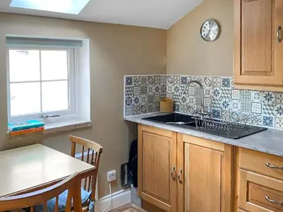 a kitchen with a sink and a table and a clock at Monawilline Cottage in Lamlash