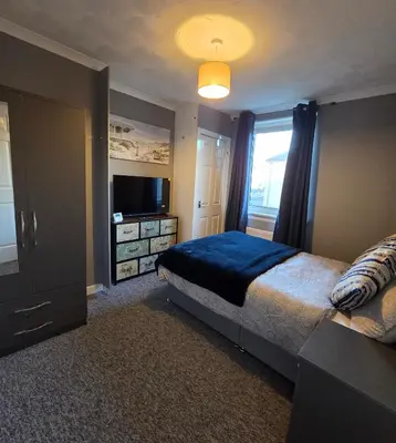 a bedroom with a large bed and a television at 3 Bedroom FM Homes & Apartments Wishaw Motherwell in Dalziel