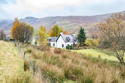 a white house on a hill with mountains in the background at Glenogle Highland Estate Home in Lochearnhead