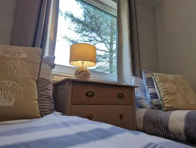 a bedroom with a bed with a lamp and a window at Ashdale Cottage with Sauna, Plunge Pool, Games Room, Kit Drying Room in Isle of Arran