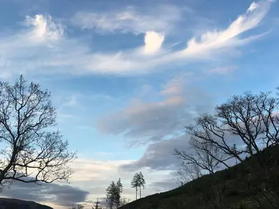 a cloudy sky with trees on a hill at Sòghail Luxury Lodge and Balquhidder Mhor with Hot Tub in Kingshouse