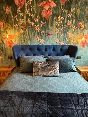 a bedroom with a blue bed with a floral wallpaper at Distillers Cottage, Peaceful rural retreat in Lanarkshire, onsite craft distillery, hot tub, bbq hut, central for exploring Scotland in Forth
