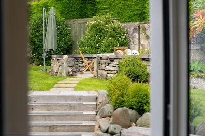 a garden with a stone wall and an umbrella at Stables Cottage in Dunira