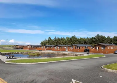 a parking lot with a pond in front of a building at Whitecairn Holiday Park in Glenluce