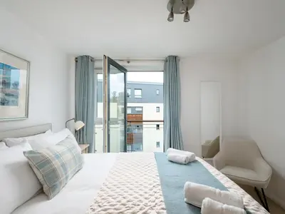 a white bedroom with a bed and a chair at Pass the Keys Spacious Bright Modern Edinburgh City Flat in Edinburgh