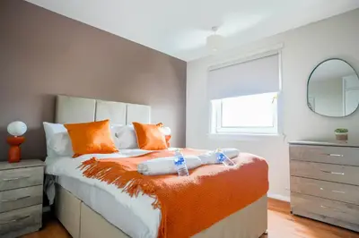 a bedroom with a bed with orange pillows and a mirror at 4 BDR House By Caledonia Luxe Stays Short Lets & Serviced Accommodation Livingston in Livingston