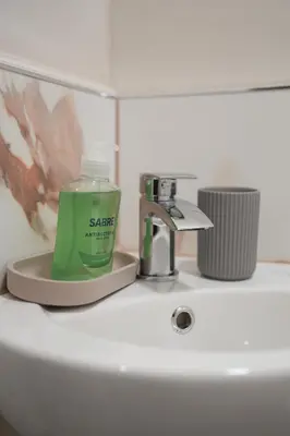 a green bottle of soap sitting on top of a bathroom sink at 4 BDR House By Caledonia Luxe Stays Short Lets & Serviced Accommodation Livingston in Livingston