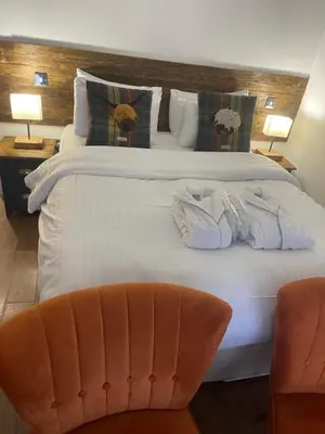 a bedroom with a large white bed with a chair at Whitemoss Lodge in Dunning