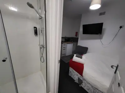 a small room with a shower and a bed and a television at Fishpond Family Suite in Moffat