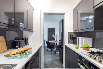a kitchen with white counters and a table with a chair at Cosy 3 bed flat in Kings Park in Glasgow