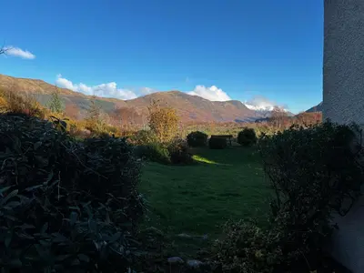 a green yard with mountains in the background at The Cottage at Craigavon House in Ballachulish