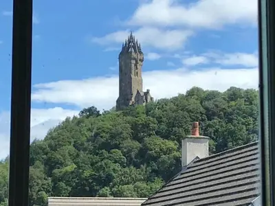 a clock tower on top of a hill with trees at Amazing Apartment by The Wallace Monument in Stirling