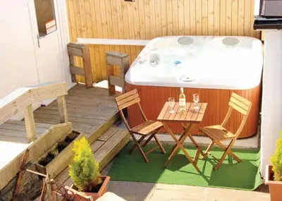 a deck with a hot tub and a table and chairs at Misty Isles Cottage- Ellenabeich, Easdale, Isle of Seil
