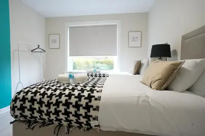 a white bedroom with a large bed with a window at Stobhill Apartment in Glasgow