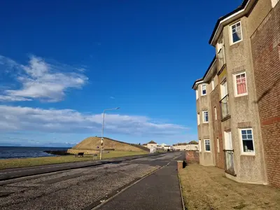 an empty street next to a building and the ocean at Seaview Retreat in Troon