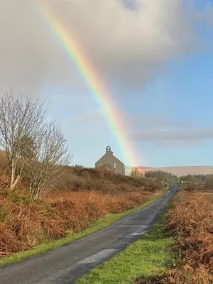 a rainbow over a road with a house on a hill at Four Woodside in Craighouse