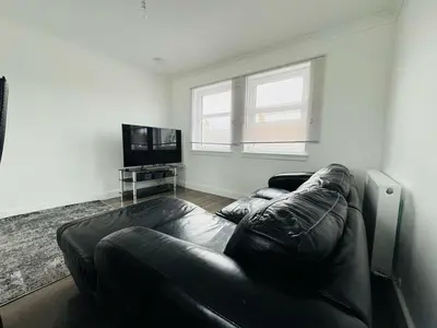 a living room with a leather couch and a flat screen tv at 3 bedroom luxury Apartment in Prestwick