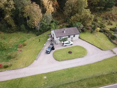 an aerial view of a house with two cars parked in a driveway at Oaktree Cottage, overlooking Loch Fyne in Cairndow