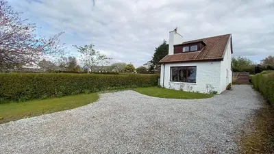 a small white house with a roof on a gravel driveway at An Cala in Connel