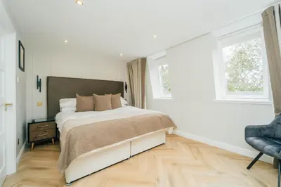 a white bedroom with a bed and a chair at Eagleside Apartments in Auchterarder