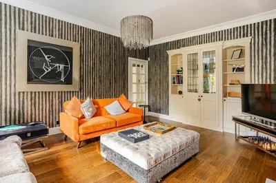a living room with an orange couch and a television at Edwardian Manor hot tub & Pool in Glasgow, Gated in Giffnock