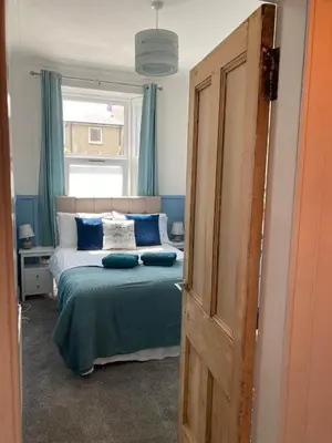 a bedroom with a bed with blue curtains and a window at The Bonnie Stay Garden Apartment in Largs