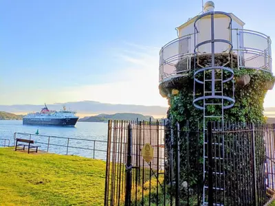 a cruise ship in the water with a lighthouse at Bay View Apartment in Oban