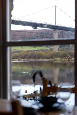 a view of a bridge from a window with a table at Cosy Lodge Getaway with Private Beach & Fireplace in Erskine