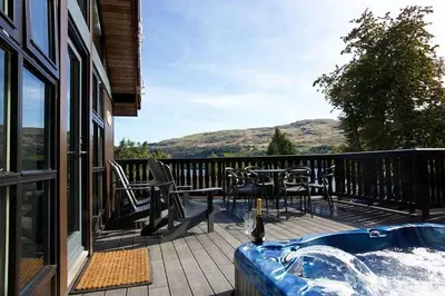 a deck with a hot tub and tables and chairs at Ardeonaig Rock in Morenish