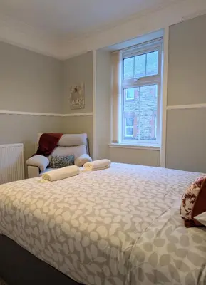 a bedroom with a bed and a chair and a window at Longrow Apartment in Campbeltown