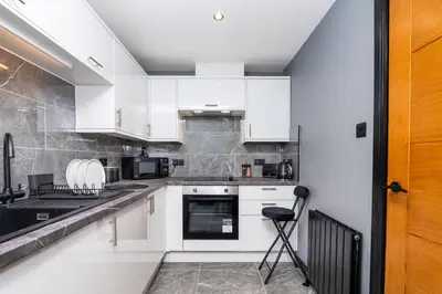 a kitchen with white cabinets and a black counter top at The Apartment in Paisley