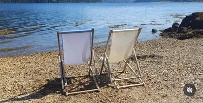 two chairs sitting on a beach next to the water at Carrick Chalets in Cairndow