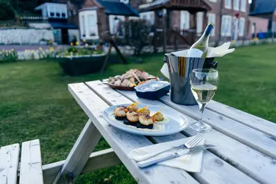 a picnic table with a plate of food and a glass of wine at The Corrie Hotel in Corrie