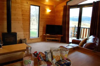 a living room with a couch and a table and a television at Woodland Oak Log Cabin, by Meall nan Tarmachan in Killin