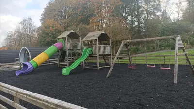 a playground with two swings and a slide at Barrhill Holiday Park - Glamping in South West Scotland - Duisk in Girvan