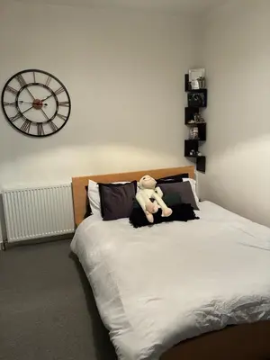 a teddy bear sitting on a bed with a clock at 2 bedroom fully furnished apartment in Springburn