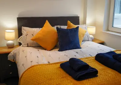 a bed with yellow and blue pillows on it at Coppet Cove - 2 Bedroom Apartment - Saundersfoot in Moffat