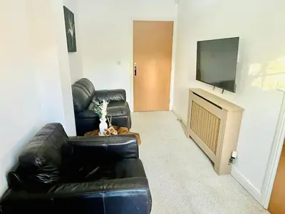 a living room with a black leather couch and a television at 3-Bedroom house near Manchester City Centre in Moffat