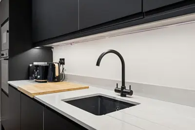 a kitchen with a sink and black cabinets at Spacious 5 Bedroom Home With 3 Bathrooms And Private Parking in Glasgow