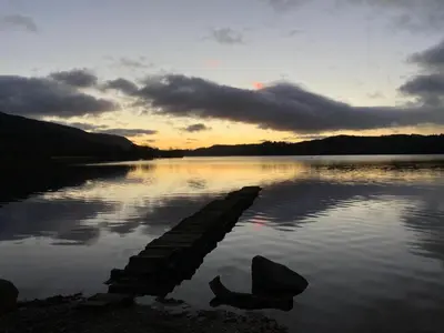 a sunset on a lake with a dock in the water at Spacious, bright home in Central Scotland sleeps 6 in Balfron