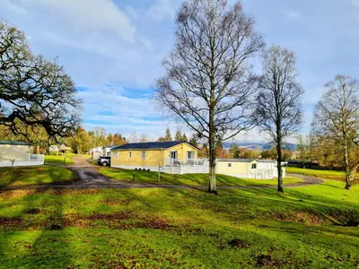 a house in a field with trees and a road at 10 lochview in Moffat