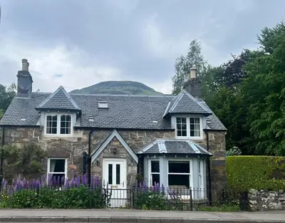 a stone house with purple flowers in front of it at Glenalbyn Cottage in Saint Fillans