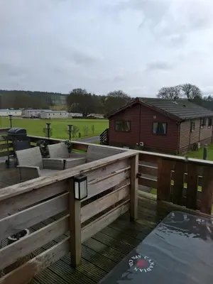 a deck with chairs and a house in the background at Redwood lodge with luxury hot tub at Three lochs holiday park in Balminnoch