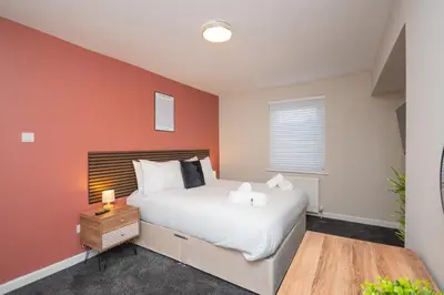 a bedroom with a white bed and an orange wall at Vacant Nests Unique 4BR home The Muirhouse in Motherwell