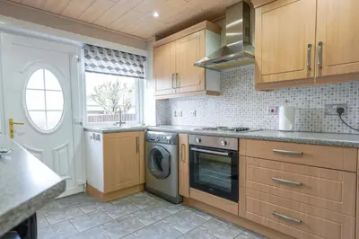 a kitchen with wooden cabinets and a washer and dryer at Jake's House in Airdrie
