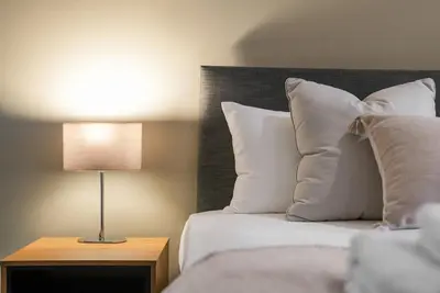 a bed with white pillows and a lamp on a table at The Snug - Beachwalk Apartments in Ayr